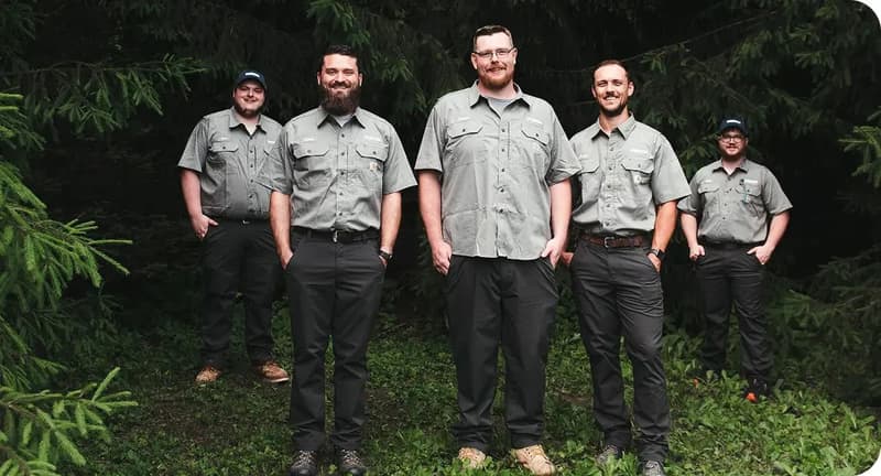 Uniformed crew of five posing outdoors among trees